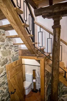 a bathroom with a toilet under a wooden staircase at CASA PITAXAN in Melide