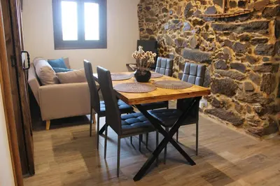 a dining room table with chairs and a stone wall at A Nosa Casa 2 in Belesar