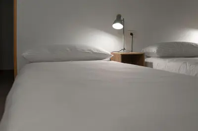 a bedroom with two beds with white sheets and a lamp at Hostal Santa Cruz in Santiago de Compostela
