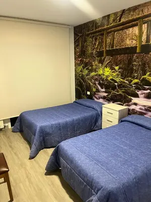 a room with three beds with blue sheets and a wall at Hostal Carpinteiras in Rodeiro