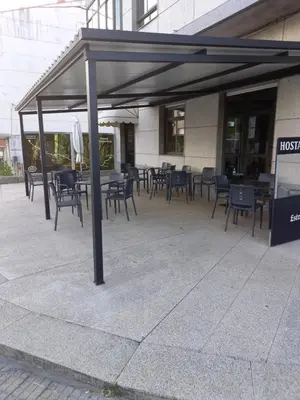 a covered patio with tables and chairs in front of a building at Hostal Carpinteiras in Rodeiro
