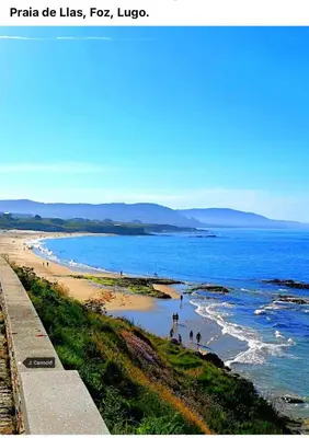 a beach with people walking in the water at O Xuncal in Barreiros