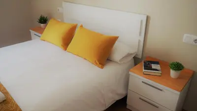 a bedroom with a white bed with yellow pillows and a table at ***** Solaina das Burgas ***** en el Casco Viejo in Ourense