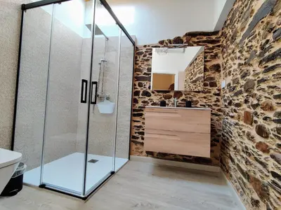 a bathroom with a glass shower and a stone wall at La Casita de la Ribeira Sacra in Monforte de Lemos