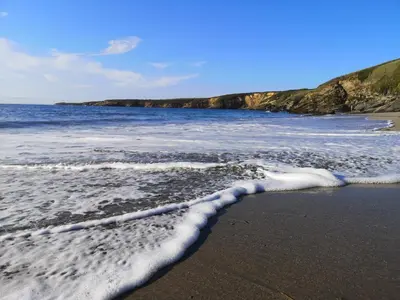 a sandy beach with foam on the water at Cabanela Maitia Apto Matteo Barbacoa in Ribadeo