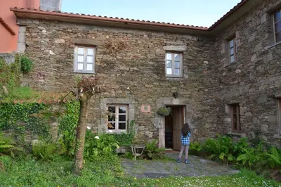 a woman standing in front of a stone house at Casa Pousadoira in Miño