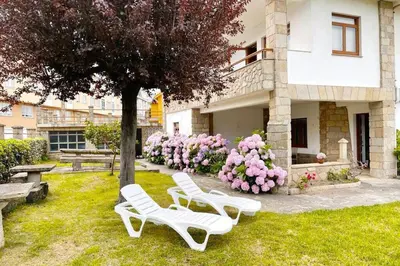 two white chairs and a tree in front of a building at Covas Beach Garden in Viveiro