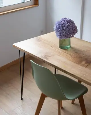 a wooden table with a vase of purple flowers and a green chair at Ferreiros - Wood Design apartments in Puentedeume