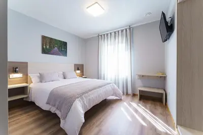 a white bedroom with a bed and a television at PENSIÓN CASA ELENA *** in Arzúa
