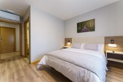a bedroom with a large white bed and wooden floors at PENSIÓN CASA ELENA *** in Arzúa