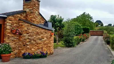 a brick house with flowers and a driveway at Casetón do Forno. in Lourenzá