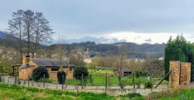 a stone house in a field with a castle in the background at Casetón do Forno. in Lourenzá