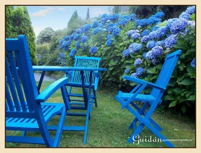 three blue chairs and a table in front of purple flowers at Apartamentos Guidan in Ribadeo