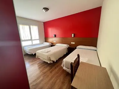 a room with three beds and a table and a red wall at Pensión Carballeira in Arzúa