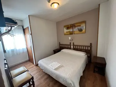 a small bedroom with a bed and a chair at Pensión Carballeira in Arzúa