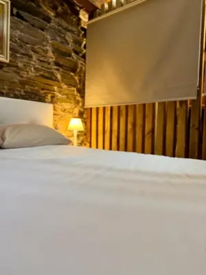 a bedroom with a white bed with a stone wall at Casa Folibar in Manzanedo de Valdueza