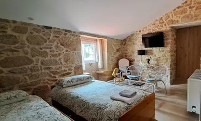 a bedroom with two beds and a stone wall at O Berce Padrón casa rural in Padrón