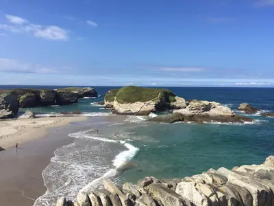 a beach with rocks and people in the water at Villa sobre el mar con acceso a la playa , ideal para familias y grupos in Ribadeo