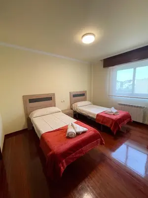 a bedroom with two beds with red sheets and a window at Alojamiento Apostol 2 in Melide