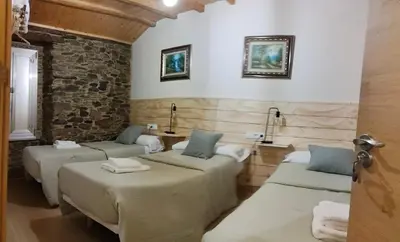 a room with four beds and a stone wall at A casa do lajueiro in Arzúa