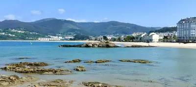 a beach with rocks in the water and buildings at Alojamientos Viveiro - Ático Playa de Covas in Viveiro