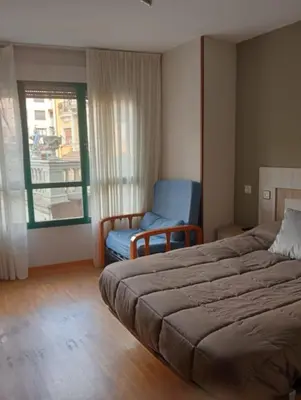 a bedroom with a bed and a chair and a window at Apartamentos xistra in Cangas del Narcea