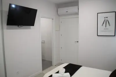 a white room with a bed and a flat screen tv at Baixo a Lua Rooming in Sarria