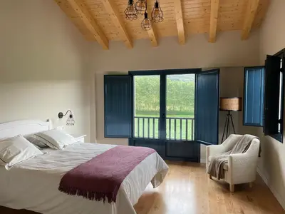a bedroom with a bed and a chair and windows at Grandes Duplex nuevos con Jardin y Barbacoa - 3 llaves, Los Gayoles Rural in Castropol