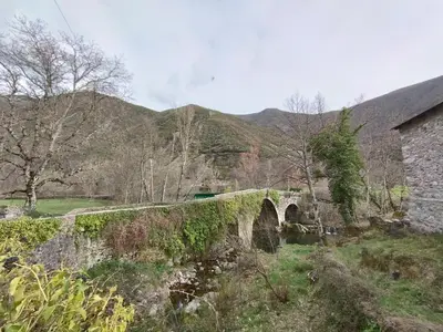 an old stone bridge over a river in a field at CAMPING LA ZARAPICA - Palacios del Sil in Palacios del Sil