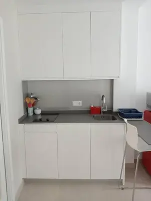 a kitchen with white cabinets and a sink and a chair at Apartamentos Tras dos Fornos in Chantada