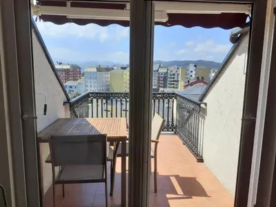 a balcony with a table and chairs and a view of a city at Atico con terraza y piscina comunitaria in Ribadeo