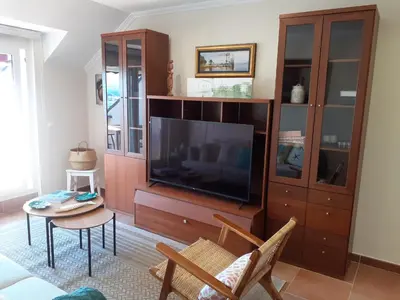 a living room with a large television and a table at Atico con terraza y piscina comunitaria in Ribadeo