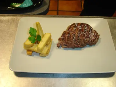 a white plate with a piece of meat and french fries at HOTEL RST. PADORNELO in Padornelo