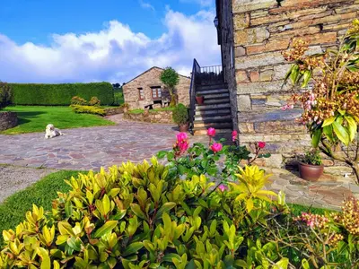 a dog sitting next to a brick building with flowers at Pajar in Braña