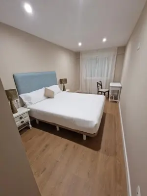a bedroom with a large white bed and wooden floors at Apartamentos Turísticos MENCÍA in Monforte de Lemos