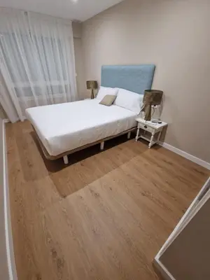 a bedroom with a white bed and a wooden floor at Apartamentos Turísticos MENCÍA in Monforte de Lemos