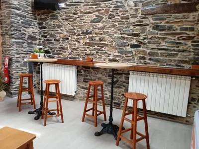 a bar with three wooden stools and a stone wall at O Lar do Alecrín in Friol