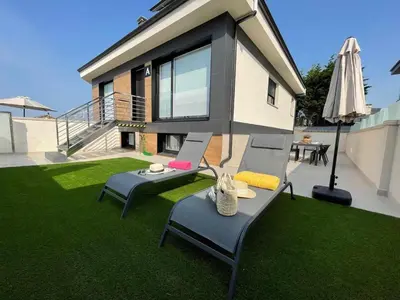 a house with a lawn with two chairs and an umbrella at Adosado A ( 5 hab) in Foz