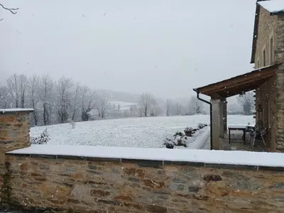 a snow covered field behind a stone building with a bench at Casa Os Prados da Albela in Tríacastela