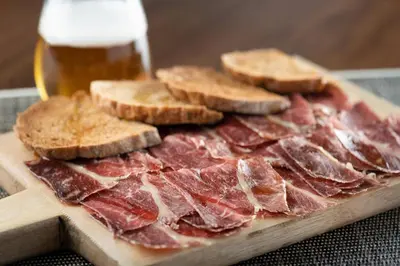 a pile of meat on a cutting board with a glass of beer at AC Hotel Ponferrada by Marriott in Ponferrada