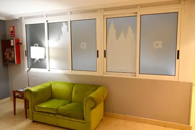 a green couch in a living room with windows at Hotel Alda San Carlos in Santiago de Compostela