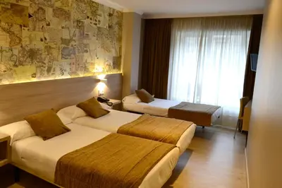 a hotel room with two beds and a window at Hotel Alda San Carlos in Santiago de Compostela
