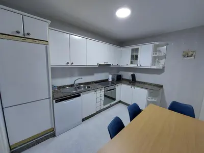 a kitchen with white cabinets and a table and blue chairs at Acea Nova 2 in Monforte de Lemos