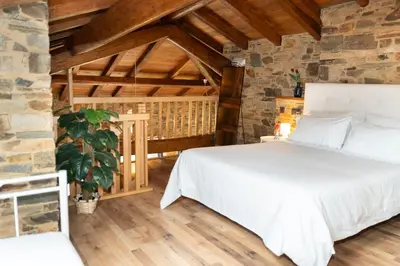 a bedroom with a white bed and a stone wall at CASA EL TEIXO in Taramundi
