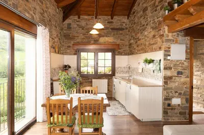 a kitchen with a table and chairs and a stone wall at CASA EL TEIXO in Taramundi