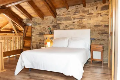 a bedroom with a white bed and a stone wall at CASA EL TEIXO in Taramundi