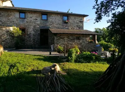 a woman sitting in the grass in front of a house at Casa de piedra en pequeña aldea de Ortigueira in Nieves