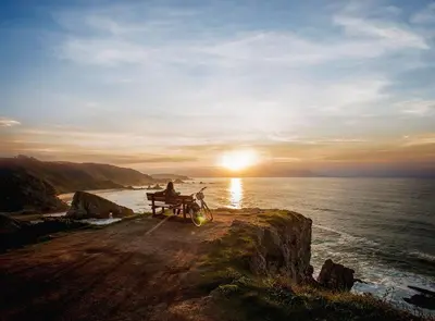 a person sitting on a bench next to the ocean at Apartamento Piscina 1G by Urraca Suites Viveiro in Viveiro