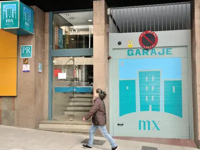 a woman walking in front of a car garage at México PR in Santiago de Compostela
