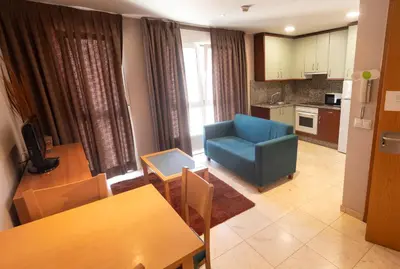 a living room with a blue chair and a kitchen at Apartamentos Ciudad de Lugo in Lugo
